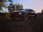 2006 Ford Mustang GT in black, showcasing sporty design and modified features on a sunset-lit street.