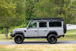 1993 Land Rover Defender 110 in Nardo Grey parked on a grassy area, showcasing off-road readiness and restoration.