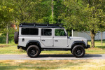 1993 Land Rover Defender 110 in Nardo Grey with black leatherette interior, parked on a grassy area.