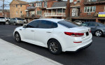 2019 Kia Optima LX sedan in pearl white parked on street with clear background, featuring alloy wheels and tinted windows.