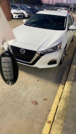 Front view of a white Nissan Altima with keys in focus, parked in a lot.