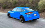 2024 Honda Civic Sport hatchback in blue parked on a road with grassy hills in the background