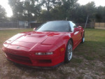 1996 Acura NSX T in red with modifications, parked in grassy area, showcasing its distinct styling.