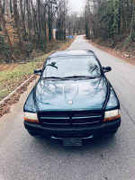 Front view of a 1997 Dodge Dakota with low miles parked on a quiet road, showcasing its V6 engine and aging paint.