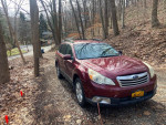 2011 Subaru Outback in red parked on a gravel road surrounded by trees, showcasing its reliable exterior.
