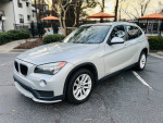 2015 BMW X1 xDrive28i AWD in silver, parked in a residential area, showcasing its clean exterior and modern design.