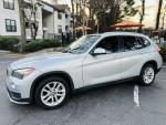 2015 BMW X1 xDrive28i AWD in silver parked near an apartment, featuring tinted windows and alloy wheels.