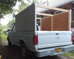 1991 Ford F150 truck with a camper shell and wooden frame, in good condition, parked in a garden.