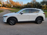 Side view of a 2019 Mazda CX-5 Touring in white parked outdoors, showcasing sleek design and alloy wheels.