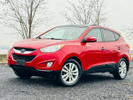 2013 Hyundai Tucson Limited in red parked outdoors, featuring alloy wheels and panoramic roof.