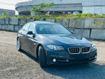 2015 BMW 5 Series 528i xDrive in gray color parked on gravel, showcasing its sleek design and modern features.