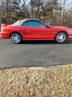 1994 Ford Mustang GT Convertible in red with low mileage, parked on a paved driveway in a natural setting.
