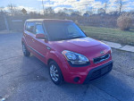 2013 Kia Soul in red, showcasing sleek design and alloy wheels, parked in a grassy area