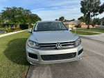 Front view of a silver Volkswagen car parked on green grass with palm trees in the background.