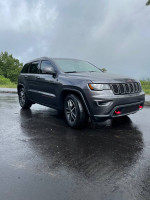 Gray Jeep Grand Cherokee Trailhawk parked on wet pavement, showcasing its rugged design and features.