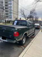 2002 Ford F150 Super Crew Cab parked, showcasing its green exterior and short bed, for sale with 92,000 miles.