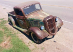 Vintage 1936 Ford pickup truck 'La Cucaracha' with unique patina and bullet holes parked by the roadside.