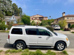White Nissan Armada parked in a residential area with lush greenery, showcasing its spacious design and excellent condition.
