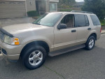 2004 Ford Explorer SUV in beige color parked in front of a house, featuring a clean exterior and 4x4 capabilities.