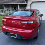 2013 Kia Rio in red color parked in front of a house with a garage.