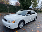 2004 Subaru Legacy sedan with 129,000 miles, parked in a leafy area, showcasing its clean exterior and sleek design.
