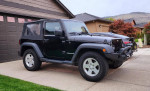 2011 Jeep Wrangler Sport 4WD parked on driveway, showcasing its off-road features and sleek black design.