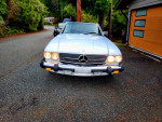 Front view of a 1986 Mercedes 560SL convertible parked on a scenic street, showcasing its classic design.