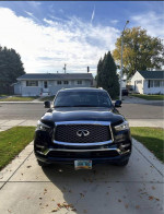 2020 INFINITI QX80 black SUV parked in driveway with clear sky and trees in the background