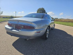Rear view of a 1997 Buick Riviera Supercharged coupe parked on a scenic road under a clear blue sky.