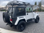 1999 Jeep Wrangler Sahara with 3-inch lift, off-road tires, and luggage rack parked on a street.