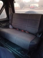 Interior view of the back seat in a 1999 Jeep Wrangler, featuring dark fabric and seat belts.