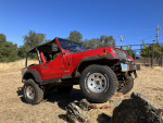 1994 red Jeep Wrangler offroad vehicle with lifted suspension and alloy wheels on boulders in a natural setting