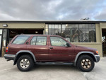 1999 Nissan Pathfinder XE RWD, maroon color, side view, parked outside with a modern building in the background.