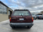 Rear view of a 1999 Nissan Pathfinder XE in maroon color, displayed in a car lot.