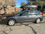 2012 Subaru Impreza 2.0i AWD hatchback with roof box and snow tires, parked in a sunny, outdoor setting.
