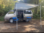 1994 Toyota Hiace SuperCustom van parked in nature with awning and chairs