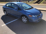 2006 Honda Civic in blue, four-door sedan with minor rear damage and gray cloth interior, parked in an open lot.