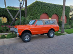 1971 Chevrolet K5 Blazer in orange with a tan soft top, parked amidst palm trees and greenery.