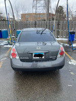 Rear view of a 2006 Nissan Altima 3.5 SE parked, showcasing minor cosmetic damage and check engine light issue.