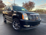 Black Cadillac Escalade with shiny chrome wheels parked outdoors, showcasing its sleek design and low mileage.