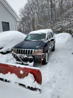 2002 Jeep Grand Cherokee with snow plow parked in snow, showcasing excellent condition and 4x4 capability.