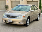 2002 Toyota Camry SE in gold color with low mileage, parked in front of garages