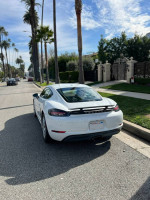2018 Porsche 718 Cayman parked on a street with palm trees, featuring a clean design and shiny finish.