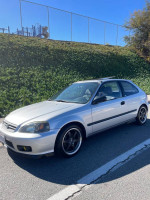 2000 Honda Civic hatchback in silver with custom wheels, parked on a street under clear blue skies.